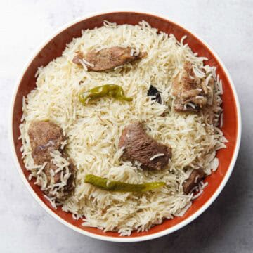 beef pulao on a plate topped with cooked chilies