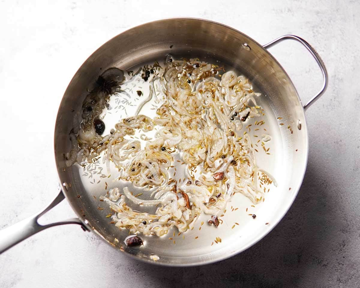 A deep pan containing sautéed onions and whole spices