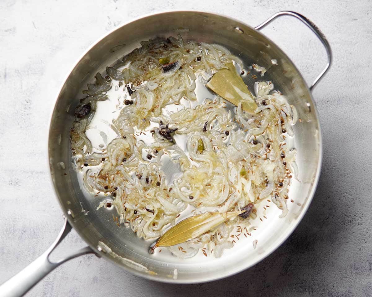 A pan with sautéed onions and whole spices in it