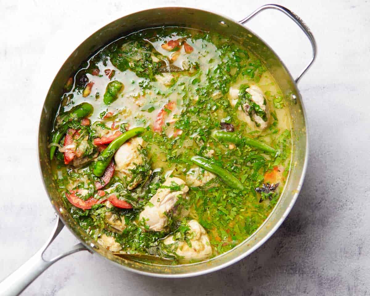 Pan filled with chicken and broth that has herbs and tomato slices