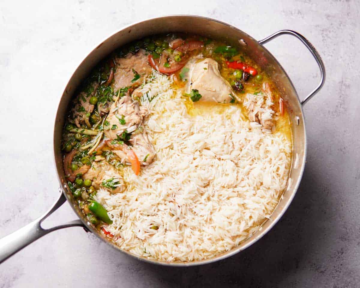 chicken pieces, green peas, herbs, tomatoes, chilies, broth, and rice in a deep pan