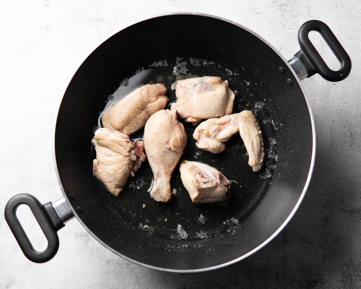 shallow fried chicken pieces in a black wok