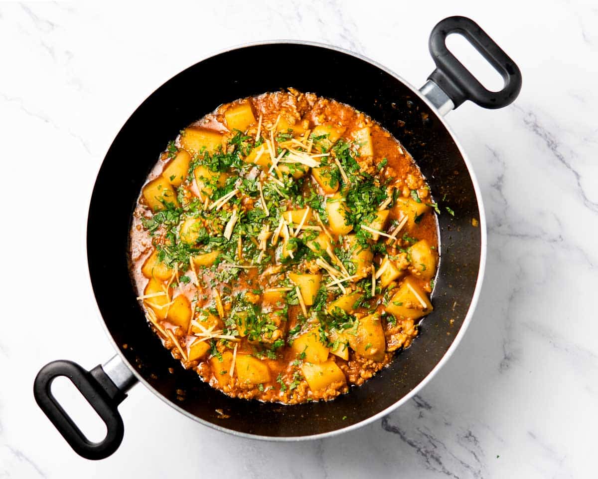 a wok containing cooked chicken aloo keema topped with herbs and ginger