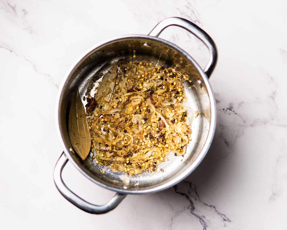 onions sautéing with spices in a stainless steel pot