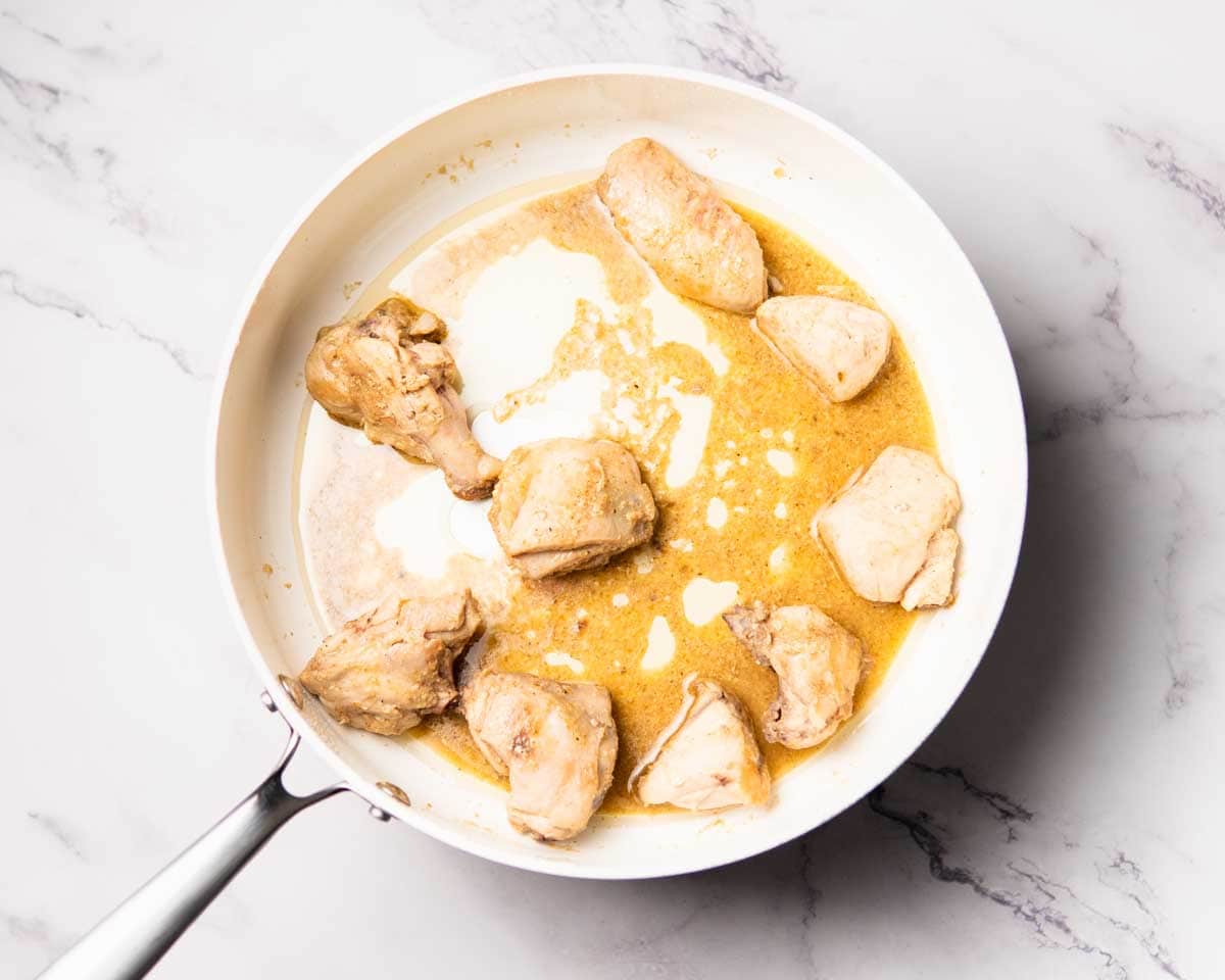 chicken cooking with yogurt, spices and aromatics in a big pan