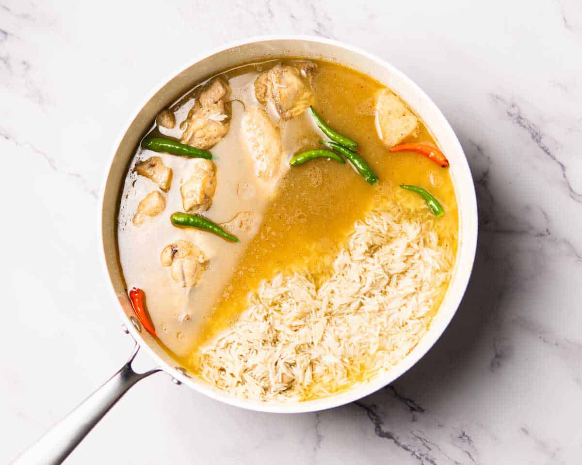 rice, chicken, yakhni and spices cooking in big, deep pan