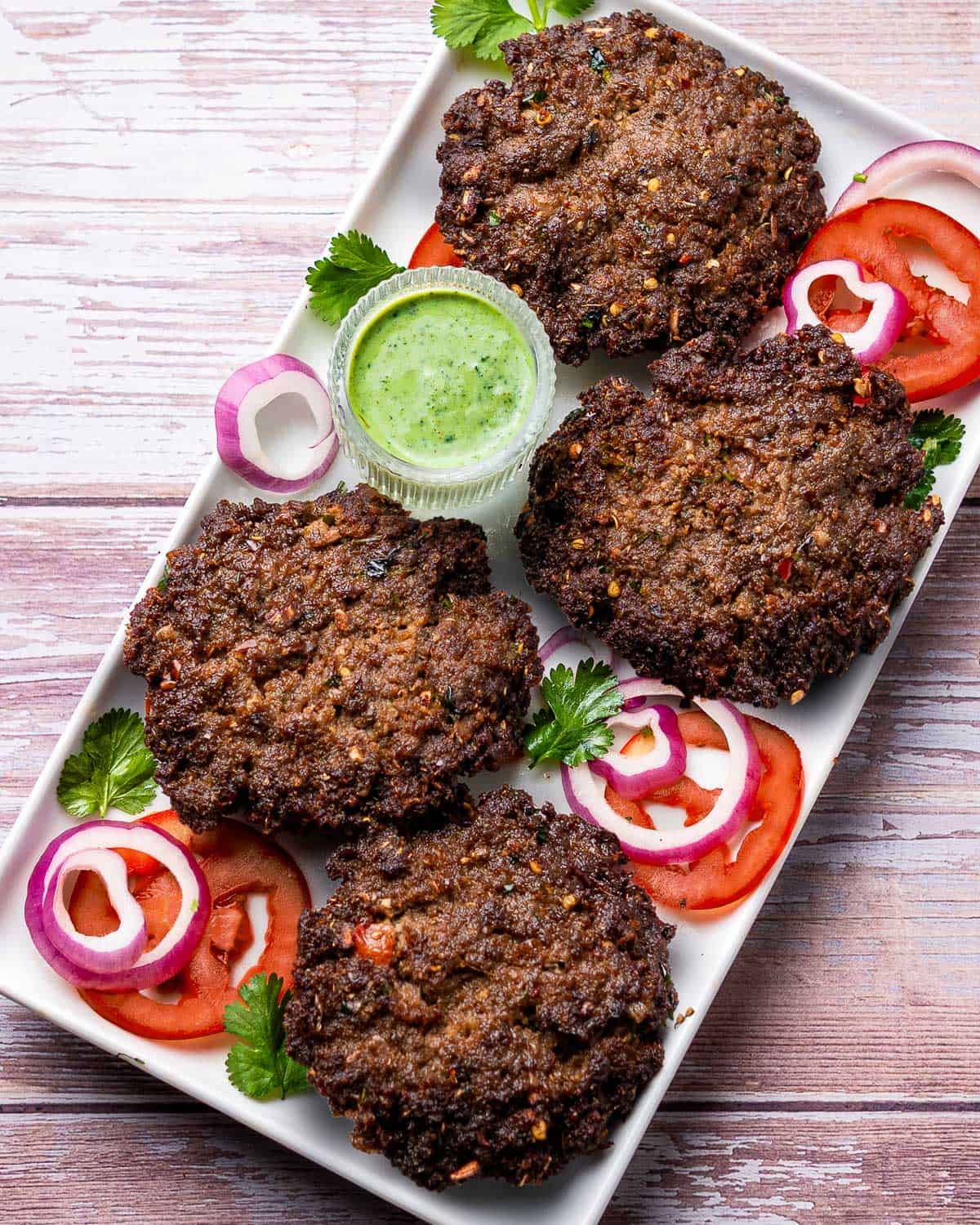 chapli kababs served on a platter with garnishes