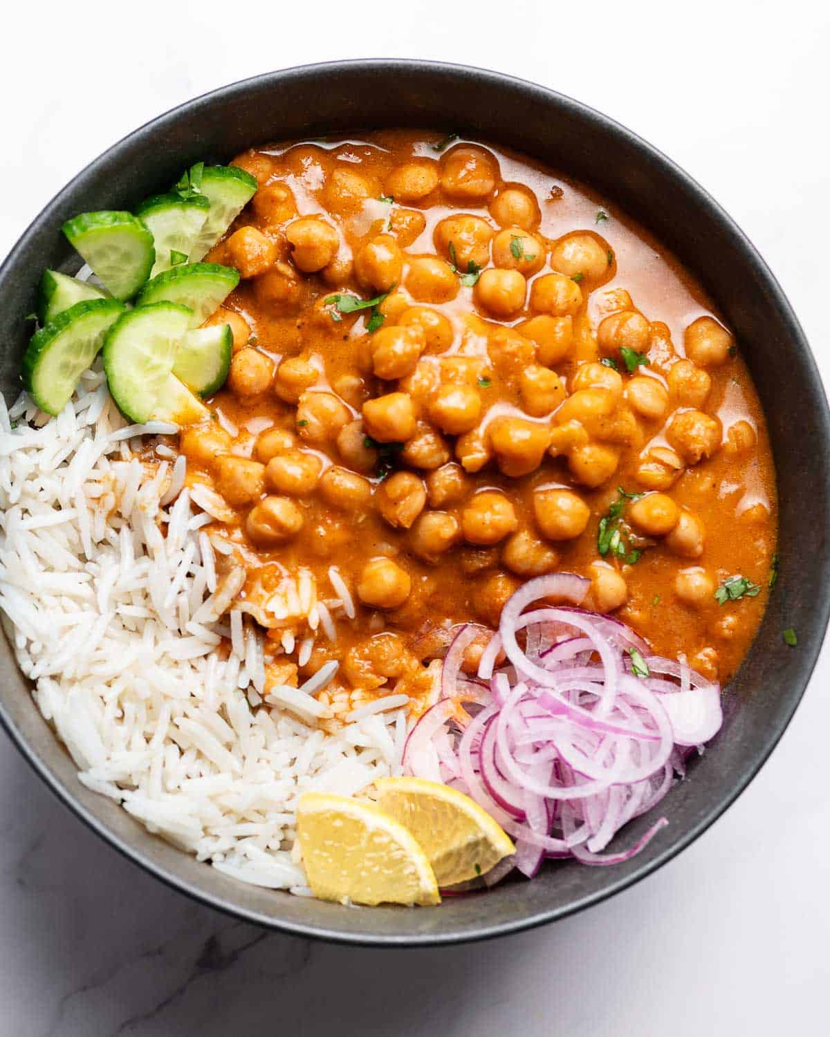 chickpea curry served with rice, onions, lemon and cucumber